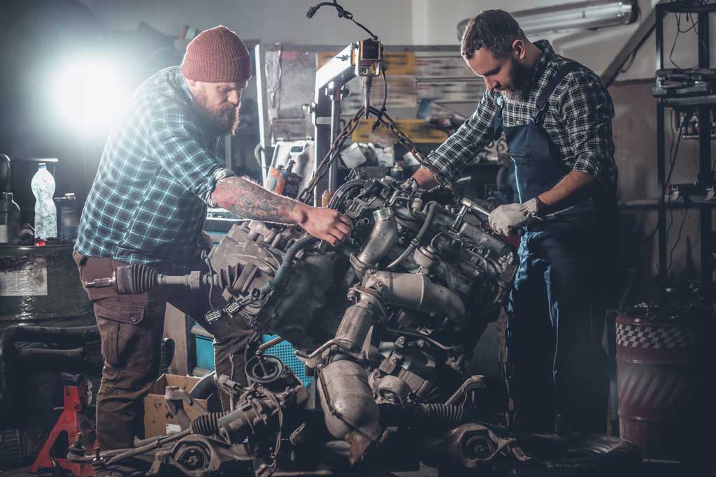 A two bearded men repairing a car in a garage and checking the engine to ensure the good condition.